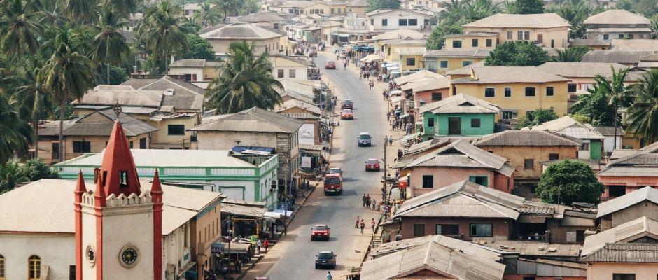 Aerial view of a coastal Ghana town with colorful houses, palm trees, and a church near the ocean