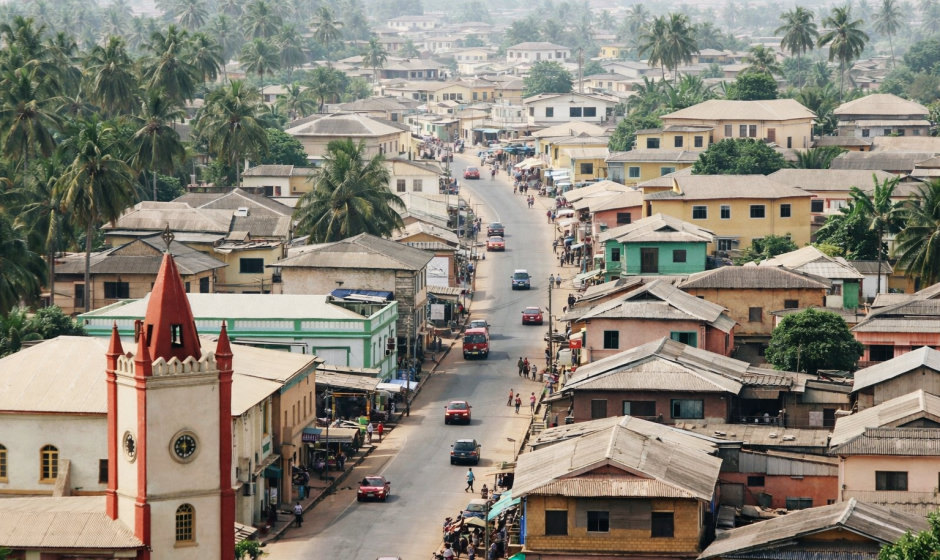 Aerial view of a coastal Ghana town with colorful houses, palm trees, and a church near the ocean