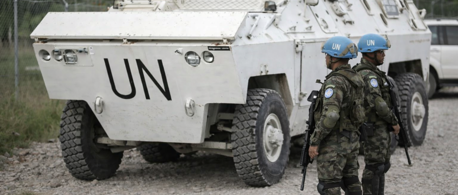 United Nations peacekeeping soldiers standing beside an armored UN vehicle on a rough road during a patrol mission