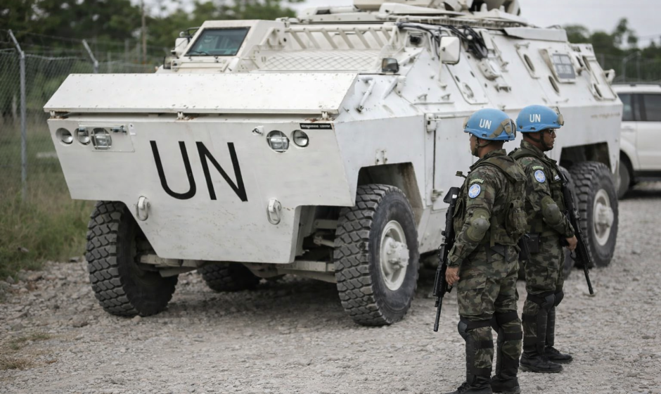 United Nations peacekeeping soldiers standing beside an armored UN vehicle on a rough road during a patrol mission