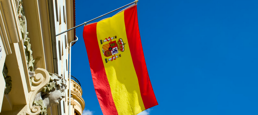 Spanish flag hanging from a building facade against a blue sky
