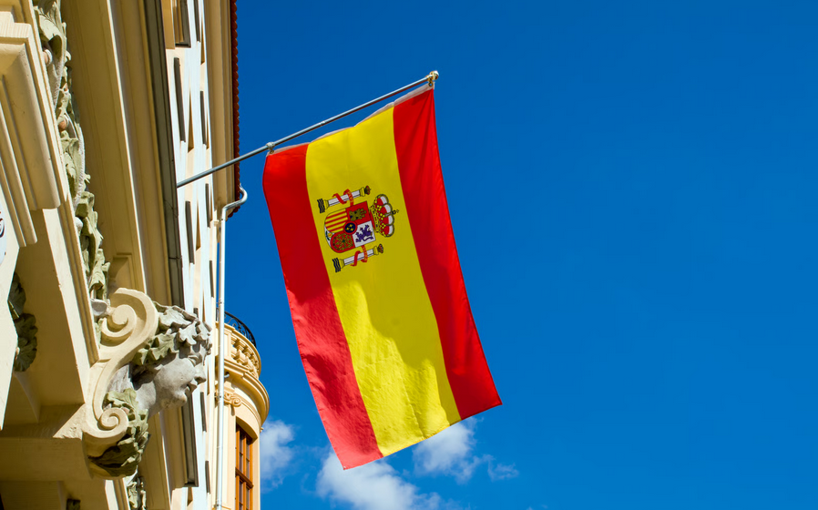 Spanish flag hanging from a building facade against a blue sky