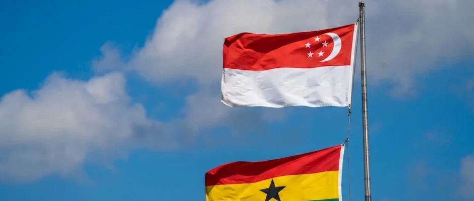 Ghana and Singapore flags flying on a flagpole against a cloudy sky