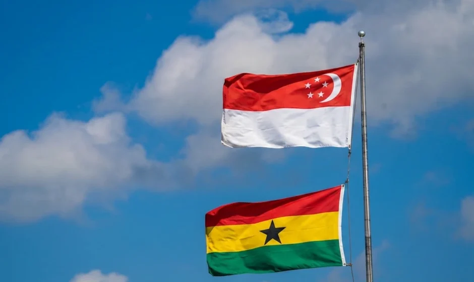 Ghana and Singapore flags flying on a flagpole against a cloudy sky