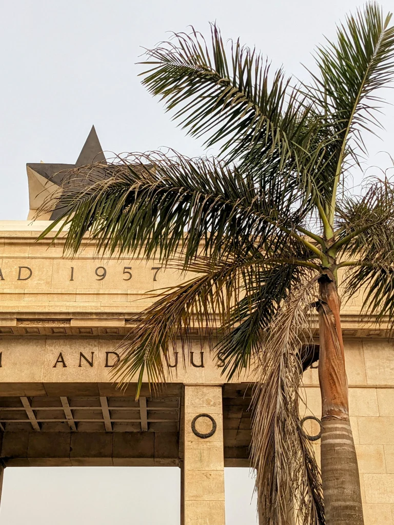 Close-up of the Independence Arch in Accra, Ghana with a palm tree in the foreground.